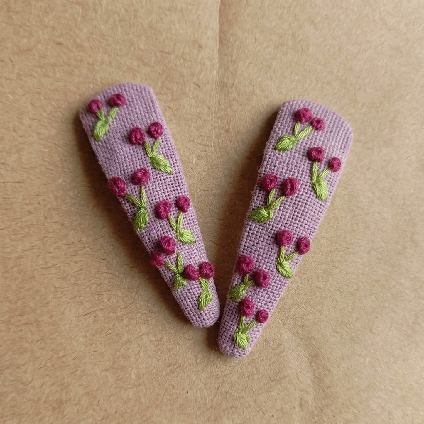 Two purple hair clips with floral designs on a brown background