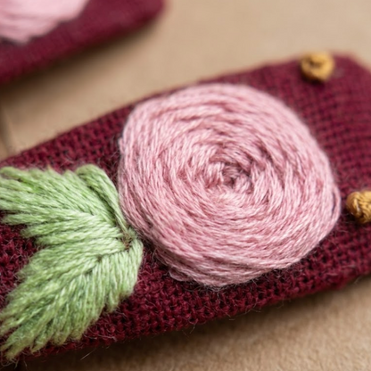 Textured fabric pouch with pink yarn rose and green leaf on a beige background