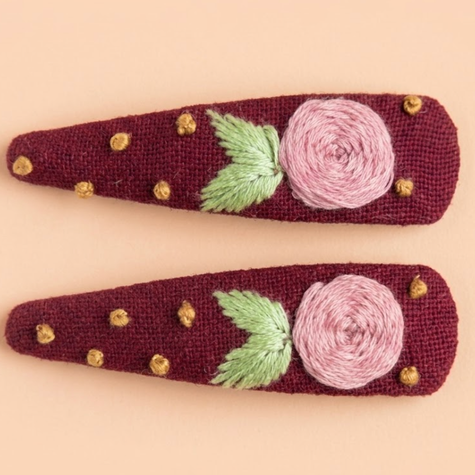 Two maroon hair clips with floral designs on a beige background
