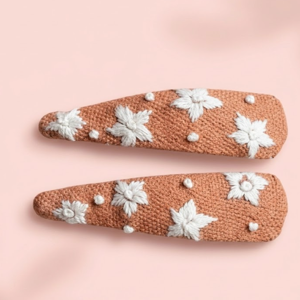 Two decorative hair clips with floral patterns on a pink background
