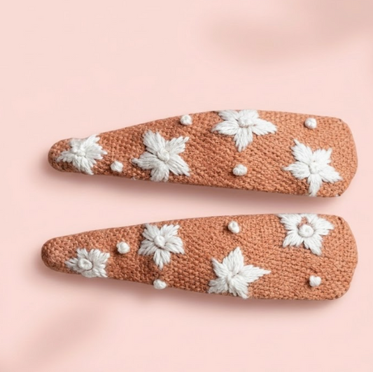 Two decorative hair clips with floral patterns on a pink background