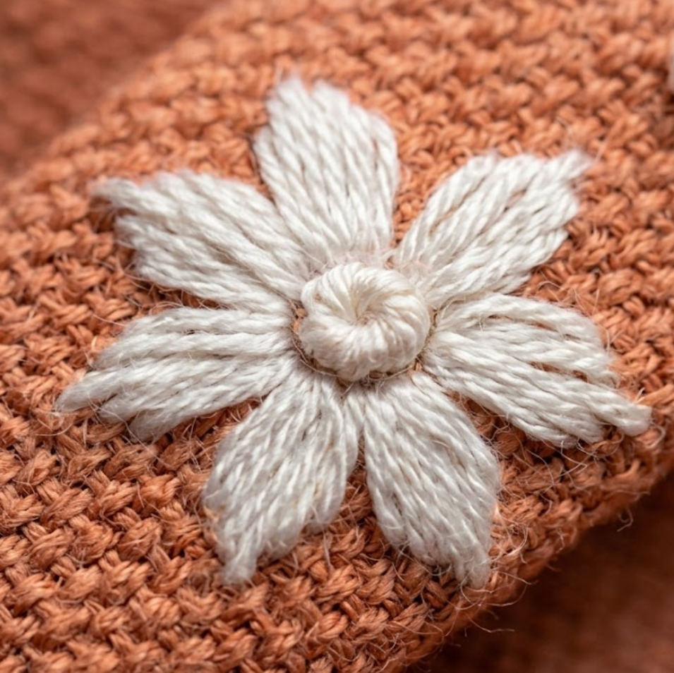 Close-up of a brown knitted fabric with a white embroidered flower.