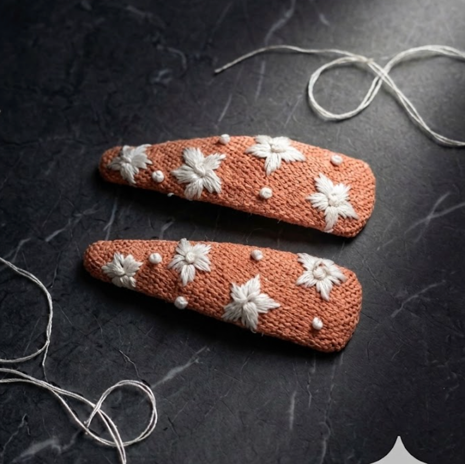 Two brown hair clips with white floral patterns on a dark surface.