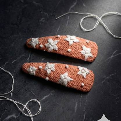 Two brown hair clips with white floral patterns on a dark surface.