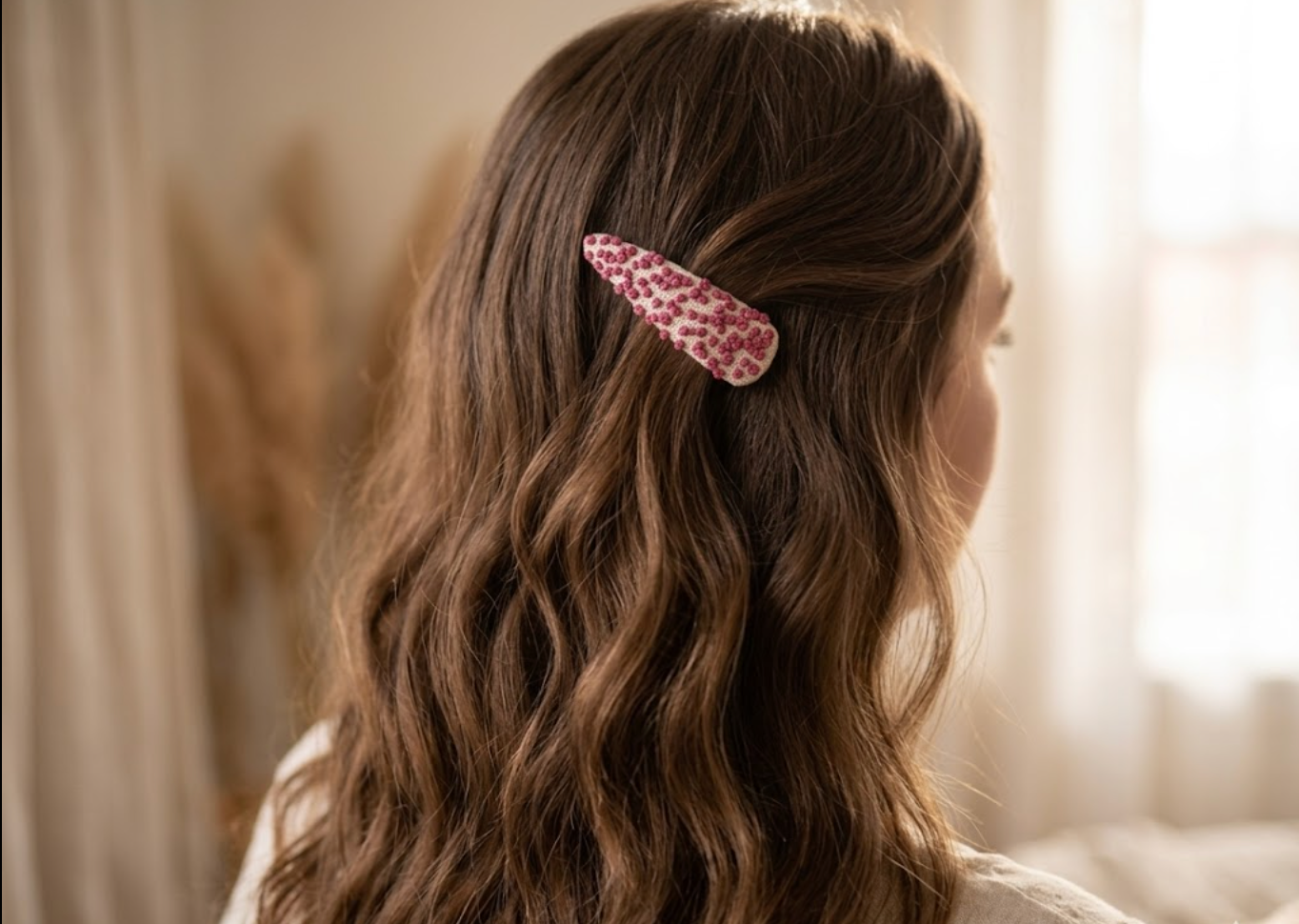 Person with wavy hair wearing a pink leopard print hair clip in a softly lit room.