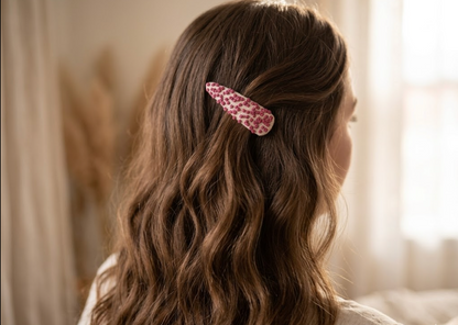 Person with wavy hair wearing a pink leopard print hair clip in a softly lit room.