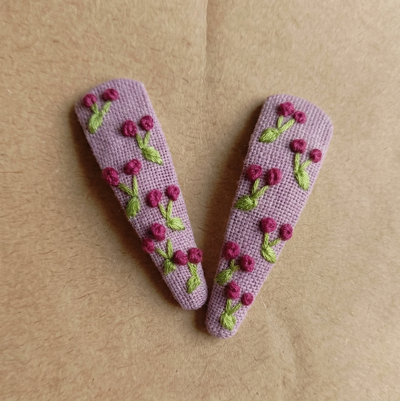 Two purple hair clips with floral designs on a brown background