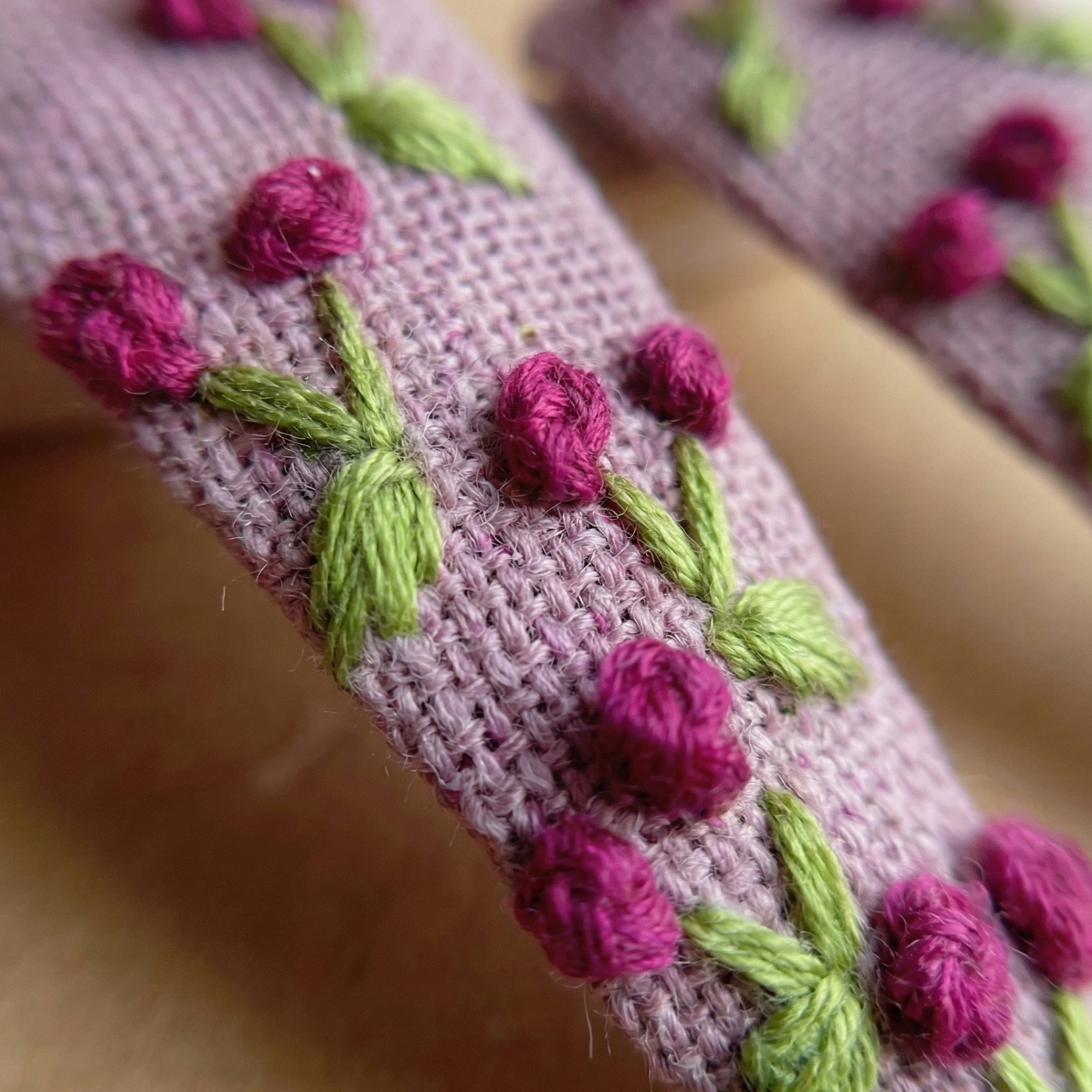 Close-up of a pink knitted fabric with embroidered pink flowers and green leaves.
