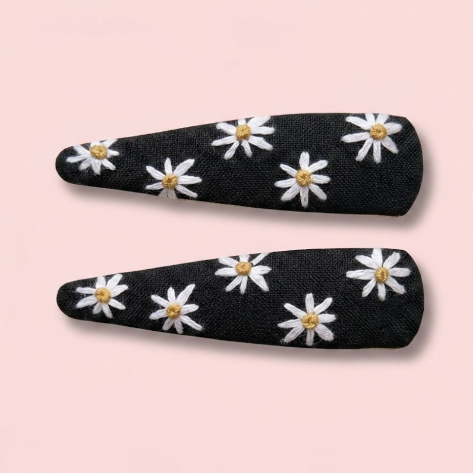 Two black hair clips with white floral patterns on a pink background