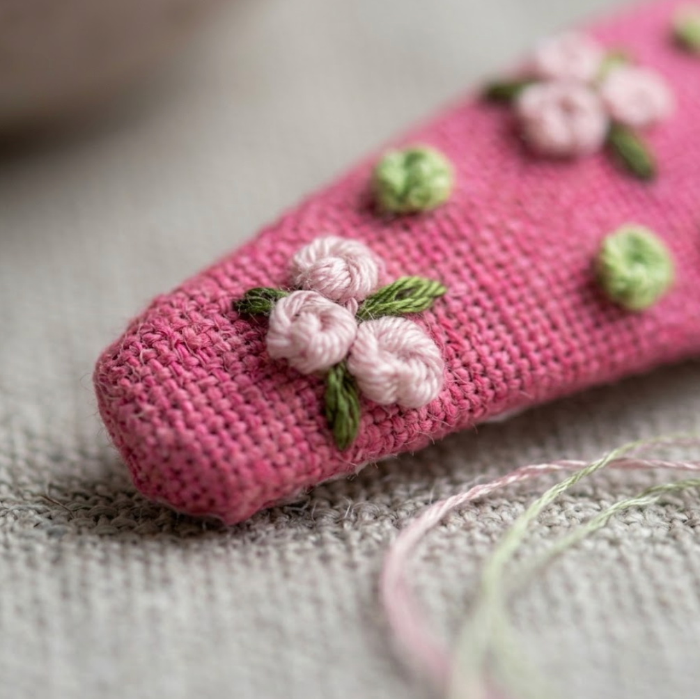 Pink knitted phone case with floral embroidery on a textured surface