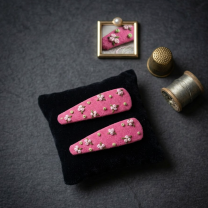 Pink hair clips with floral embellishments on a black stand, with a thimble and spool of thread in the background.