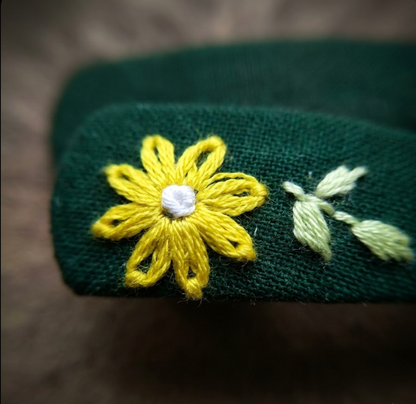 Green fabric with a yellow embroidered flower and leaves on a brown background