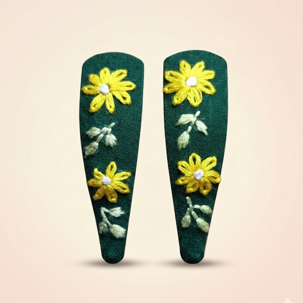 Two green hair clips with yellow floral designs on a beige background
