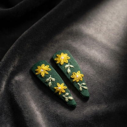 Green hair clips with yellow floral designs on a dark fabric background